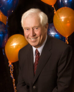 A photo of Dr. Robert Westbury from 2008 with balloons in the background. PolicyWise is honouring the visionary leadership.