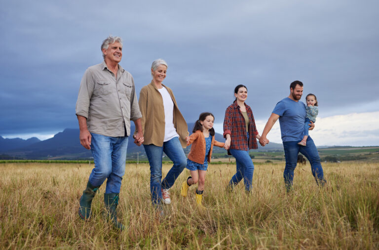 An image of a big happy family walking on field, meadow and countryside in nature to relax, bond and holding hands in love, trust and support. This image is associated with PolicyWise for Children & Families Rural Mental Health project