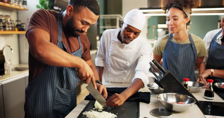 Master chef is teaching a new employee how to chop onions. Image for PolicyWise's news story titled. Building inclusive workplaces across Alberta’s food and beverage sector