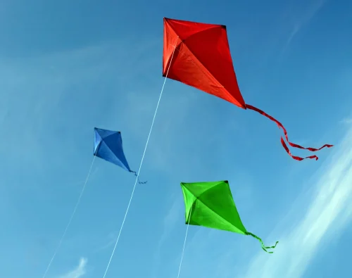 Red, blue, and green kites flying in a blue sky. This image is being used by PolicyWise for Children & Families for their news story "Leading the shift from evidence to impact."