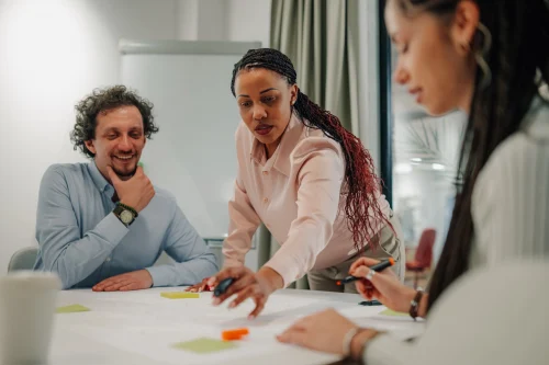 Three people working around a table looking over a strategy. This image is being used by PolicyWise for Children & Families for their news story "Leading the shift from evidence to impact."